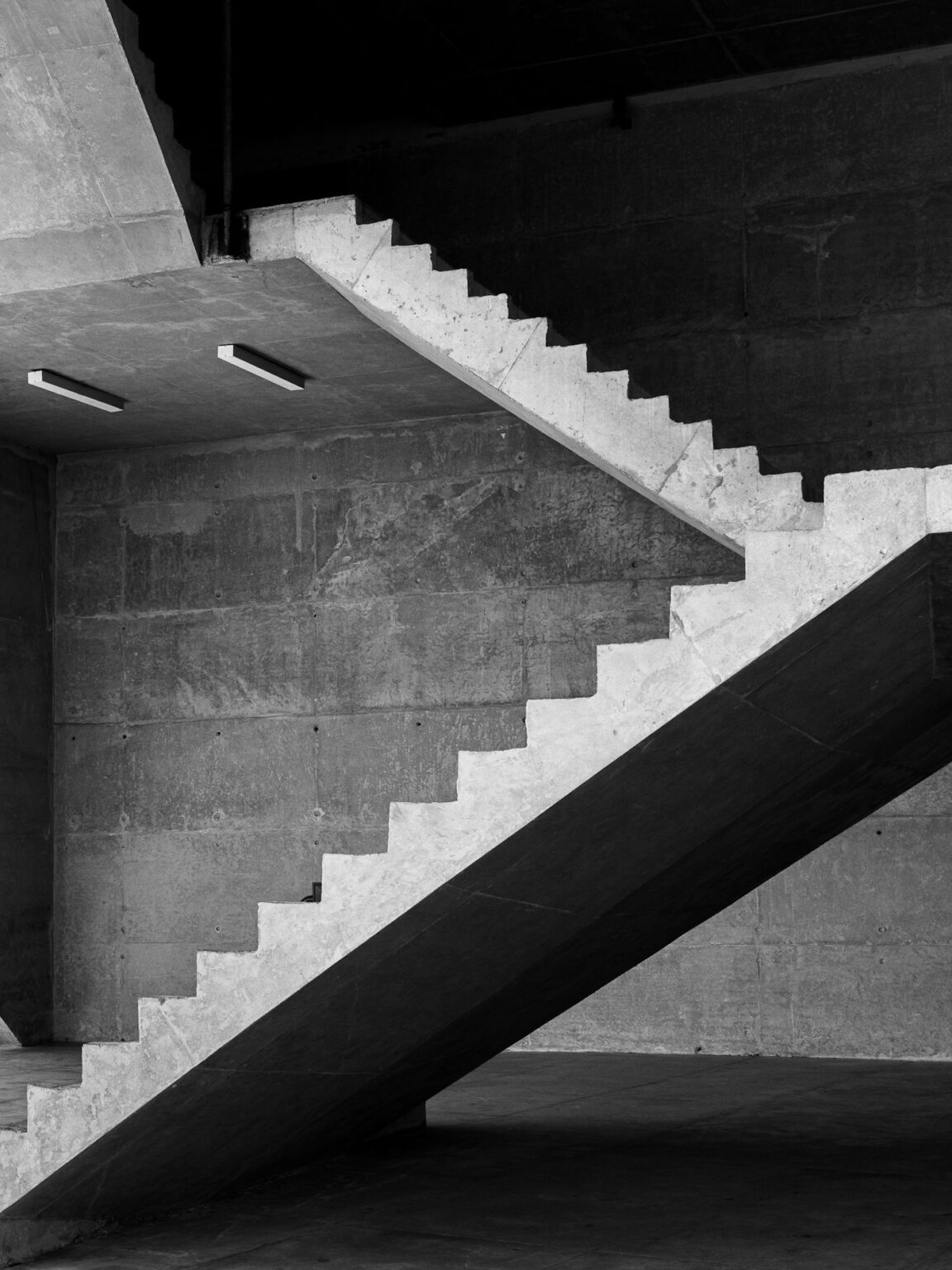 Black and white view of a concrete stair rising beside a textured wall